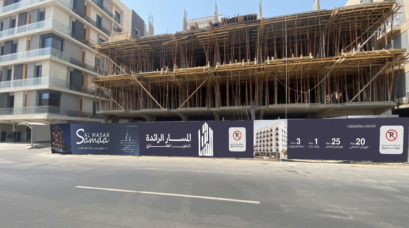 سور موقع بناء مطبوع بهوية مشروع عقاري أمام الهيكل الخرساني على شارع تجاري بجدة