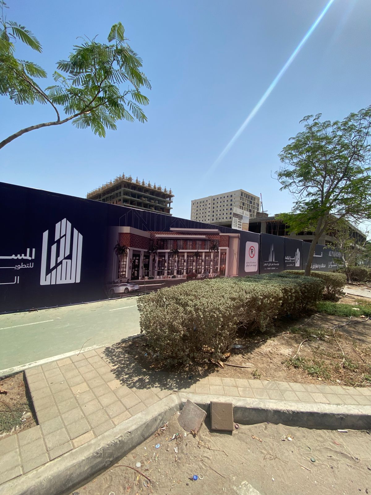 تغليف موقع بناء يعرض تصميم المبنى المستقبلي خلف سياج نباتي على الشارع