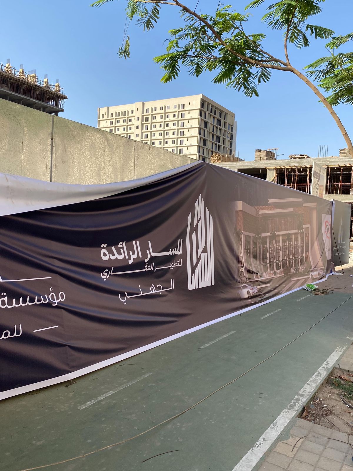تغليف مطبوع لموقع بناء يمتد على طول الرصيف وخلفه مبانٍ قيد الإنشاء