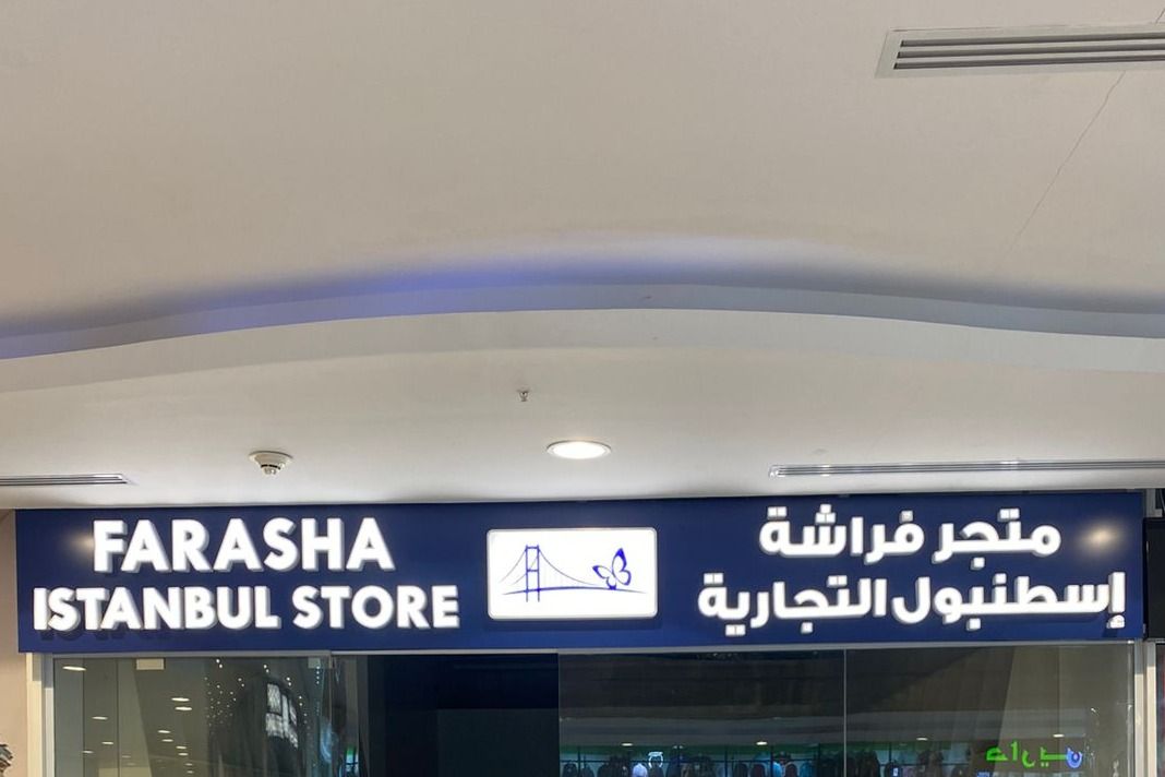 واجهة محل مضيئة بحروف بارزة بيضاء على لوح أزرق داخل مجمع تجاري