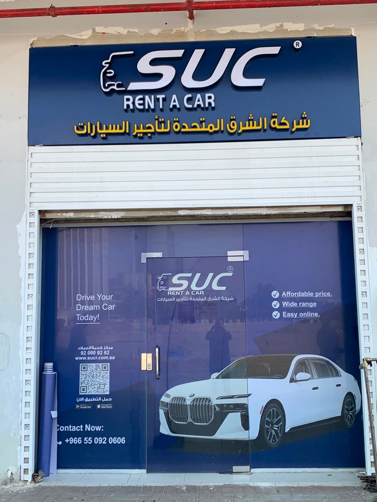 واجهة محل تأجير سيارات بلوحة علوية زرقاء ورسومات مطبوعة على الباب الزجاجي، مثال على لوحة محل، جدة