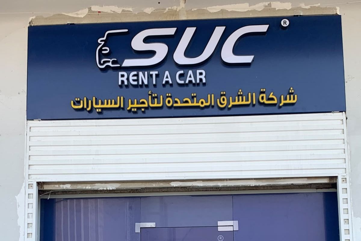 لوحة واجهة مكتب تأجير سيارات بحروف بارزة بيضاء وصفراء على لوح أزرق فوق المدخل، جدة